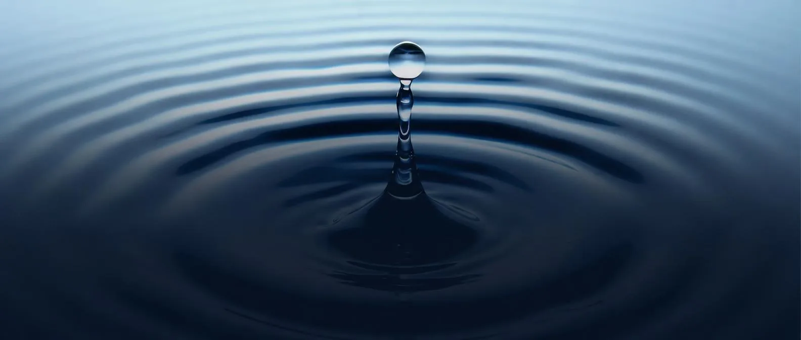 A single water droplet rippling a calm dark surface